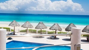 A pool area with a view of the ocean, thatched umbrellas, and lounge chairs. - Villa Marlin, Cancun Caribe, Ocean front (Cancún)