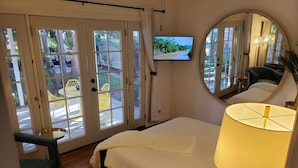 A bedroom with a bed, a TV, a mirror, and a view of the outdoors through large glass doors.