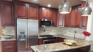 A modern kitchen with dark wood cabinets, stainless steel appliances, granite countertops, and pendant lighting.