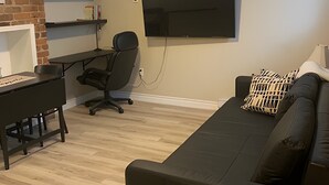 Ett modernt vardagsrum med en svart lädersoffa, ett skrivbord med en dator, en väggmonterad platt-TV och en tegelvägg som accent.