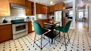 A modern kitchen with wooden cabinets, stainless steel appliances, and a dining area with green chairs. - Nice Condo in Limoilou (Quebec City)