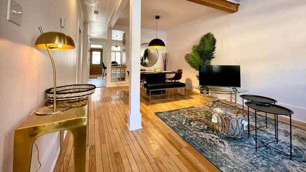 A spacious living area with a wooden floor, a flat-screen TV, and a dining area with a modern table and chairs. - Nice Condo in Limoilou (Quebec City)