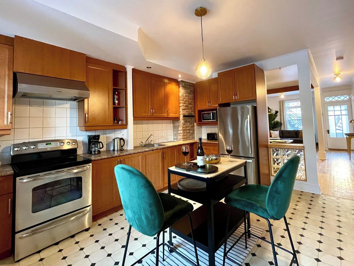 A kitchen with wooden cabinets, a black countertop, two teal chairs, and a dining table.