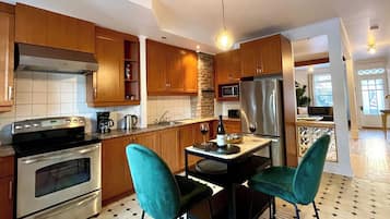 A kitchen with wooden cabinets, a black countertop, two teal chairs, and a dining table.