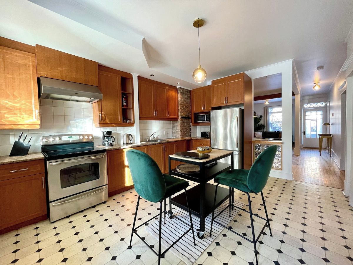 A kitchen with wooden cabinets, stainless steel appliances, and a dining area with green chairs.