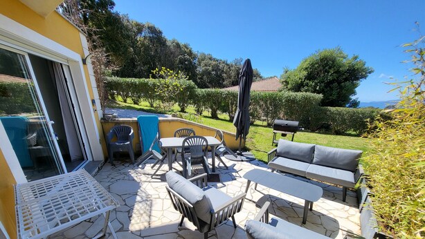 Une terrasse extérieure avec un sol en pierre, un ensemble de canapés, des chaises, une table et un barbecue.