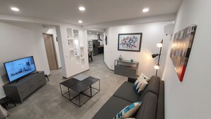 Un salon moderne avec un téléviseur à écran plat, un canapé, une table basse et un coin repas à l’arrière-plan.