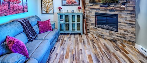 A cozy living room with a blue sofa, a fireplace, and a TV mounted on the wall.