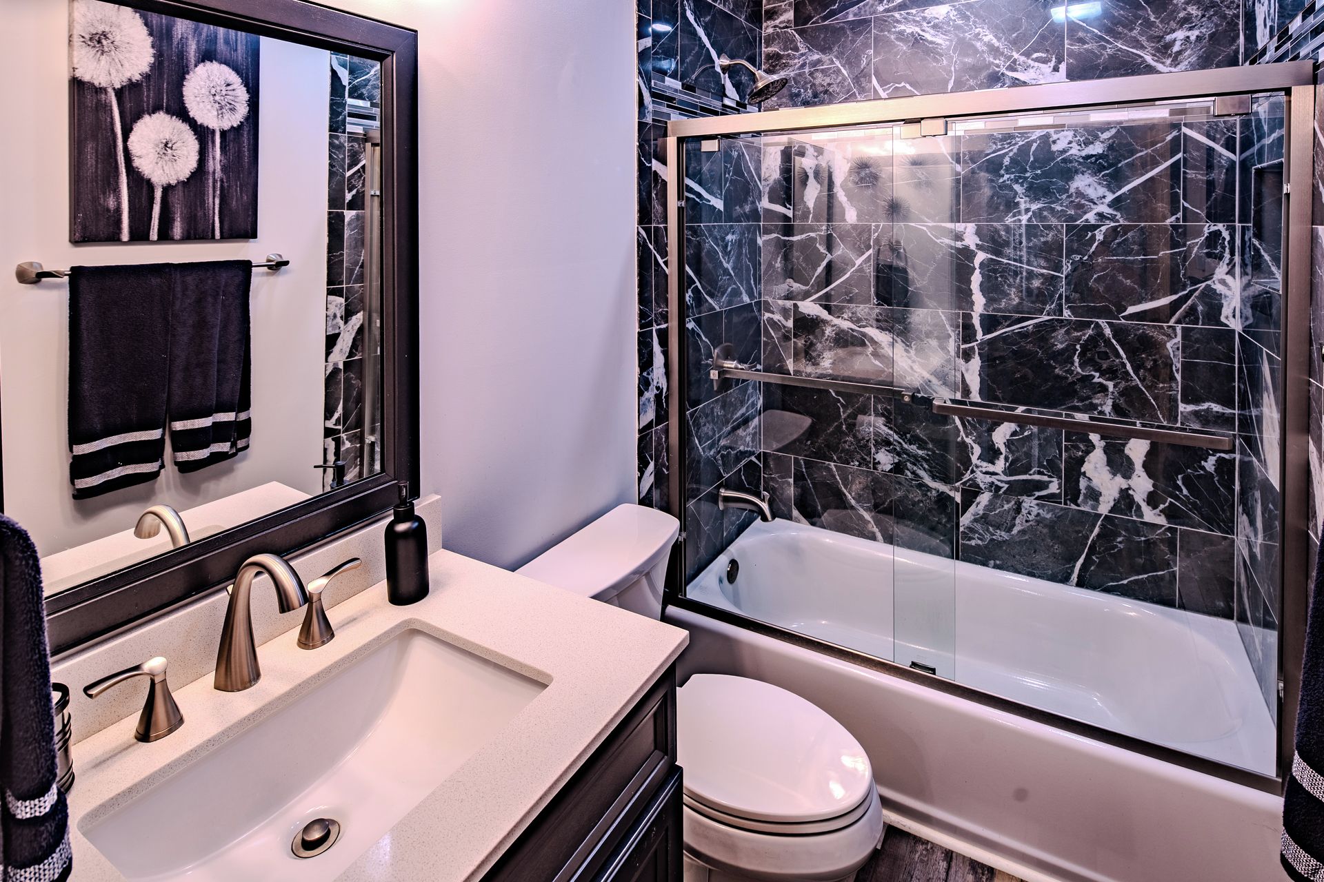 A modern bathroom with a marble shower, a sink with two faucets, and a toilet.