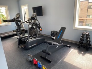 Ein Fitnessraum mit Cardiogeräten, einer Bank und Kettlebells.