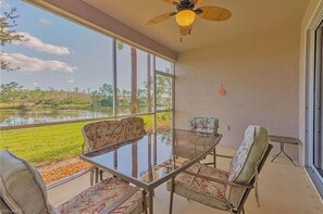 Enjoy a peaceful retreat with a glass table and comfortable seating area overlooking a serene body of water and lush greenery.
