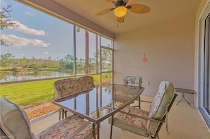 Enjoy a peaceful retreat with a glass table and comfortable seating area overlooking a serene body of water and lush greenery.