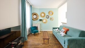 A living room with teal walls, a teal armchair, a teal sofa, a wooden coffee table, and a fireplace. - Confort et élégant, proche du parc des expositions (Paris)