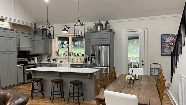 A modern kitchen with grey cabinets, a central island, wooden stools, and a dining table with chairs. - 20 min to Bryant Denny Stadium! 5min to public boat landing at Lake Tuscaloosa! (Northport)
