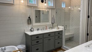 A modern bathroom with a large mirror, grey cabinets, a shower with white tiles, and a small window. - 20 min to Bryant Denny Stadium! 5min to public boat landing at Lake Tuscaloosa! (Northport)