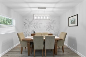 A dining room with a wooden table, six chairs, a chandelier, and a wall mural.
