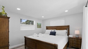 Une chambre à coucher avec un lit en bois, des murs blancs et une table de chevet avec une lampe.