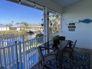 A covered porch with a view of a water body and houses in the background.