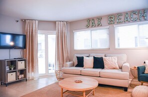 Una sala de estar con un sofá color beige, un televisor y un letrero en la pared que dice "JAX BEACH".