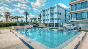 Et moderne hotel med swimmingpool, flere balkoner og en klar blå himmel.