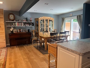 A kitchen with a dining area, wooden cabinets, a piano, and a bookshelf.