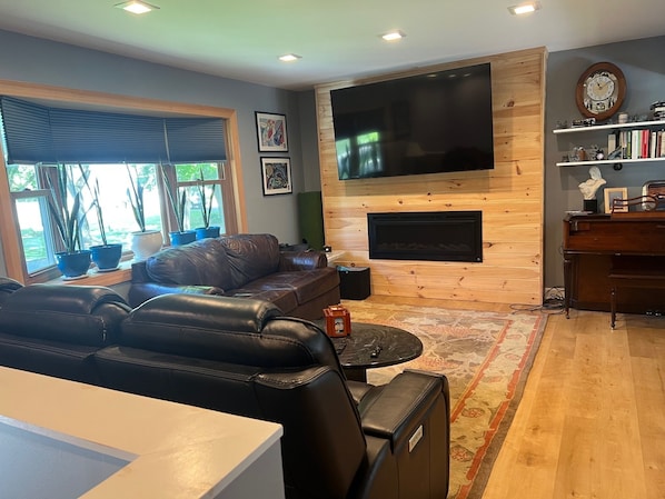 A living room with a leather sofa, a flat-screen TV, a fireplace, and a bookshelf.