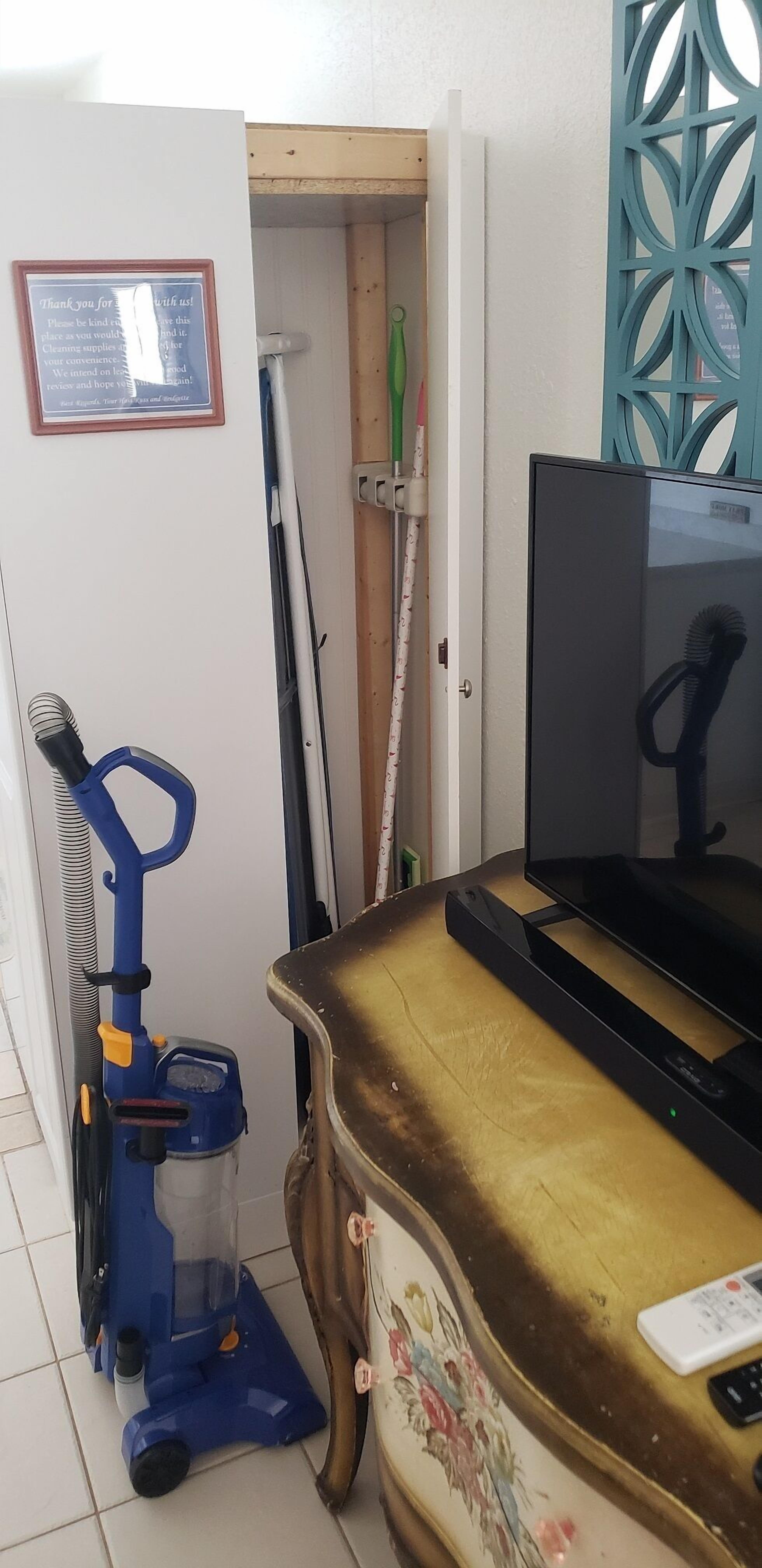 Una habitación con un escritorio, una computadora, una aspiradora, una escoba y un trapeador.