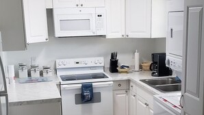Eine kleine Küche mit weißen Schränken, einer Mikrowelle, einem Herd, einem Kühlschrank und einer Kaffeemaschine.