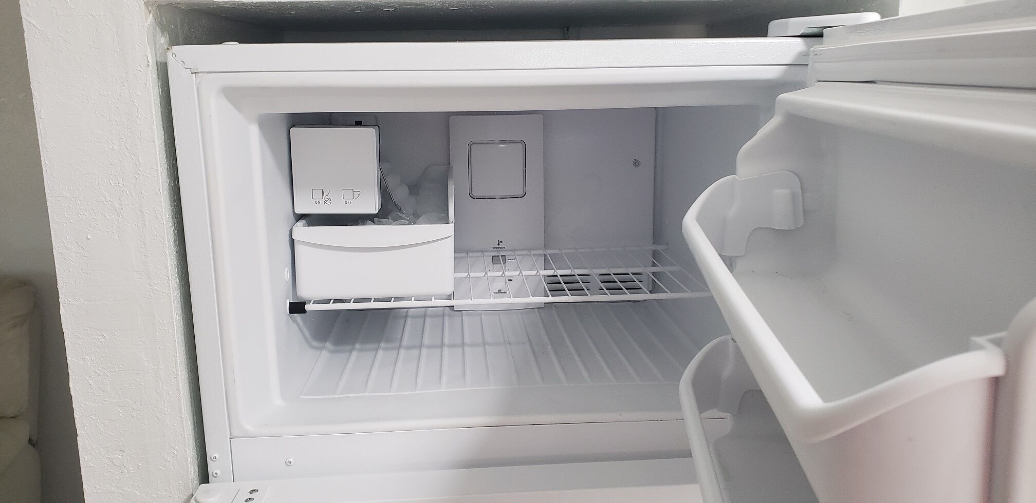 An open refrigerator with a water dispenser and a small freezer compartment.