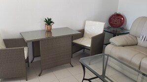 Ein kleiner Wohnbereich mit einem Glastisch, zwei Korbstühlen, einer Couch und einem kleinen Beistelltisch mit einer Dekoration.