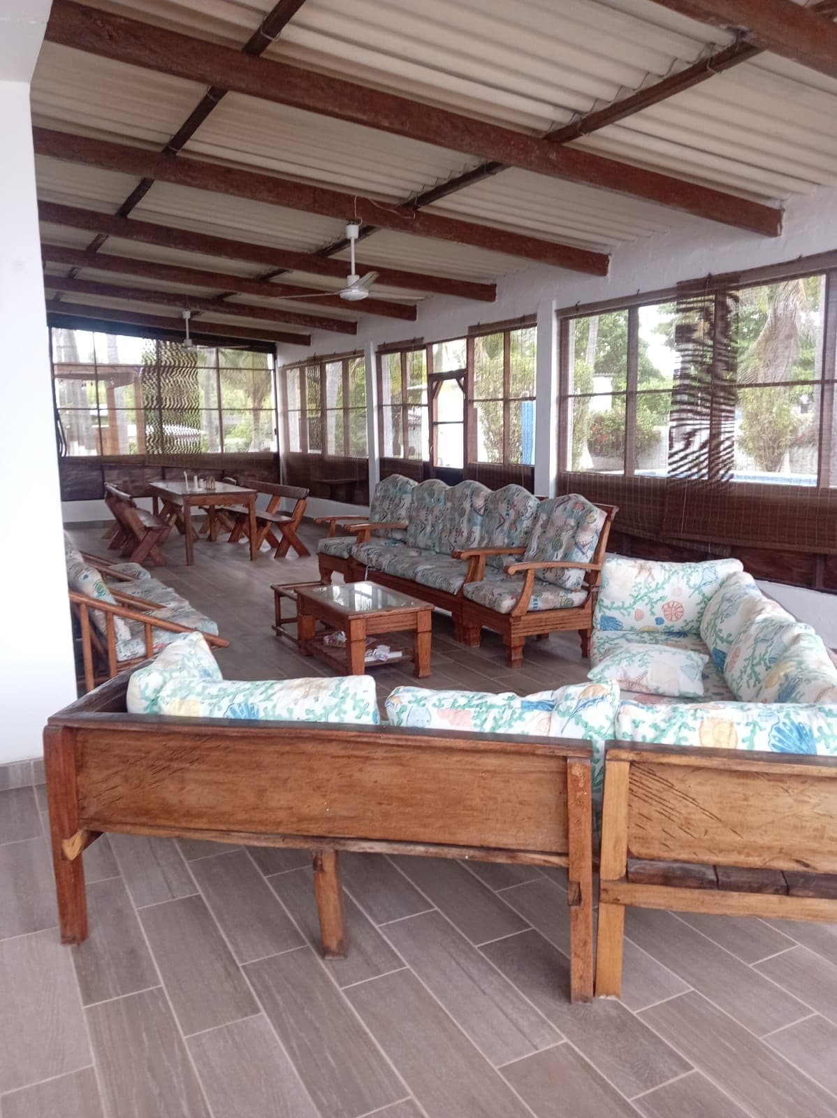 A covered outdoor seating area with wooden furniture and a tiled floor.