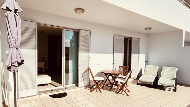 A balcony with a table and chairs, a sliding door, and a covered area with an umbrella. - Apartment “Golden View” (Porto Santo)