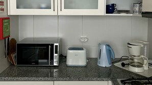 A kitchen with white cabinets, a microwave, a toaster, a kettle, and a stove. - Apartment “Golden View” (Porto Santo)