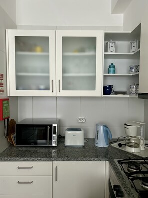 A kitchen with white cabinets, a microwave, a toaster, a kettle, and a stove.