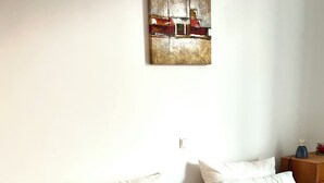 A hotel room with two beds, a wooden nightstand, a small table, and a wall-mounted artwork. - Apartment “Golden View” (Porto Santo)