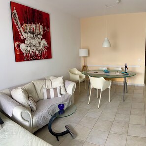 A modern living room with a sofa, a glass coffee table, a dining table with chairs, a lamp, and a painting on the wall. - Apartment “Golden View” (Porto Santo)