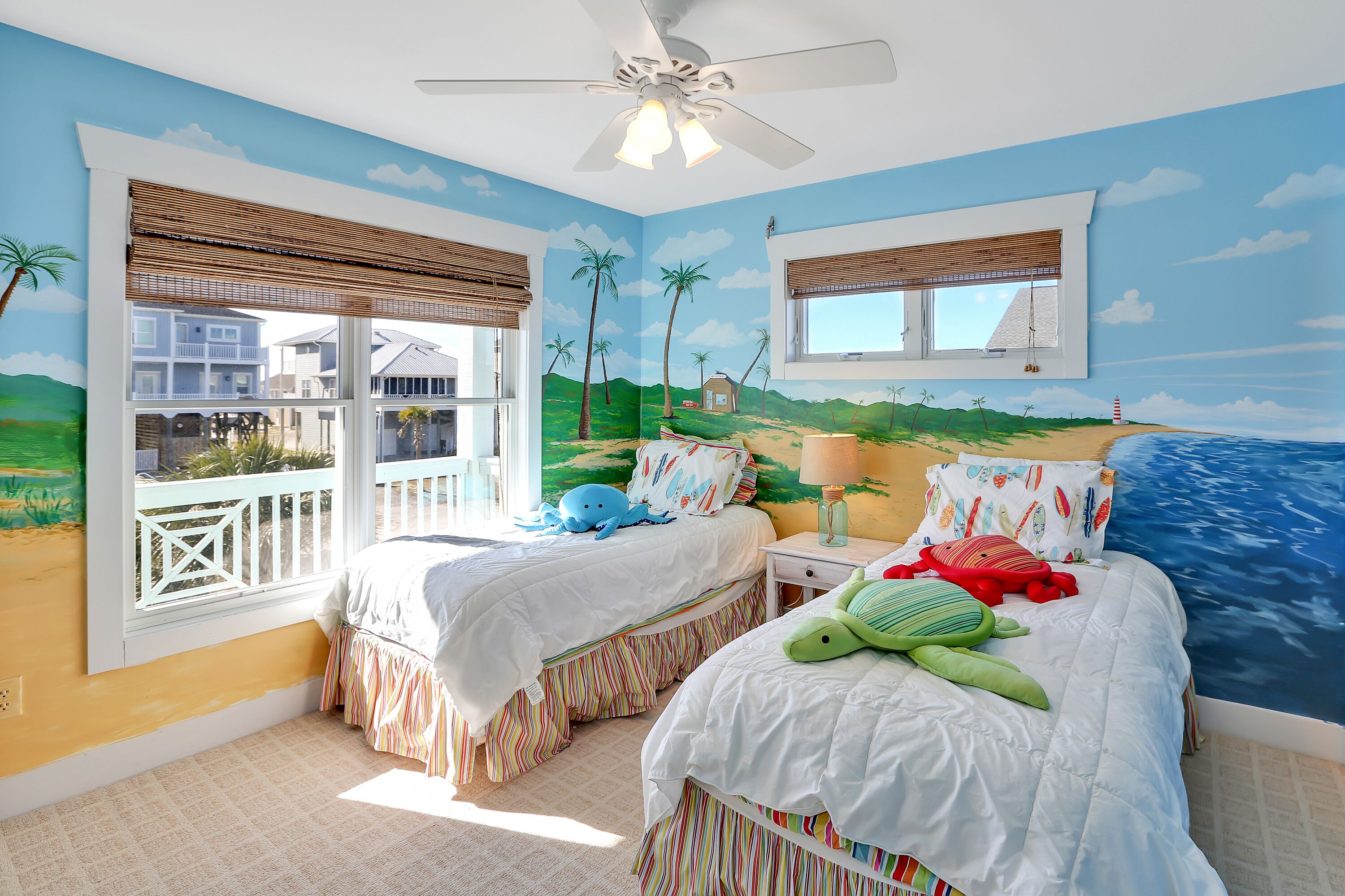Un dormitorio con dos camas, ventilador de techo y un mural con una playa.