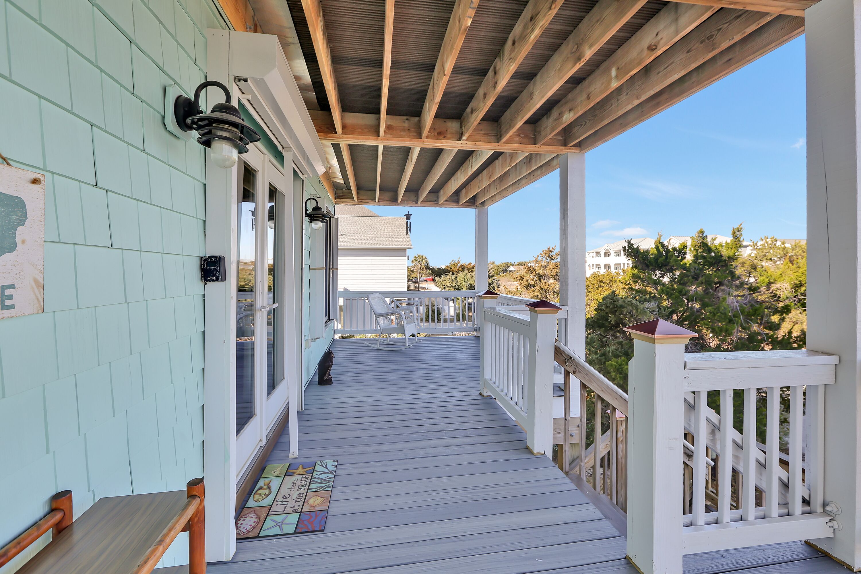 A covered porch with a wooden railing, a bench, and a view of the surrounding landscape.