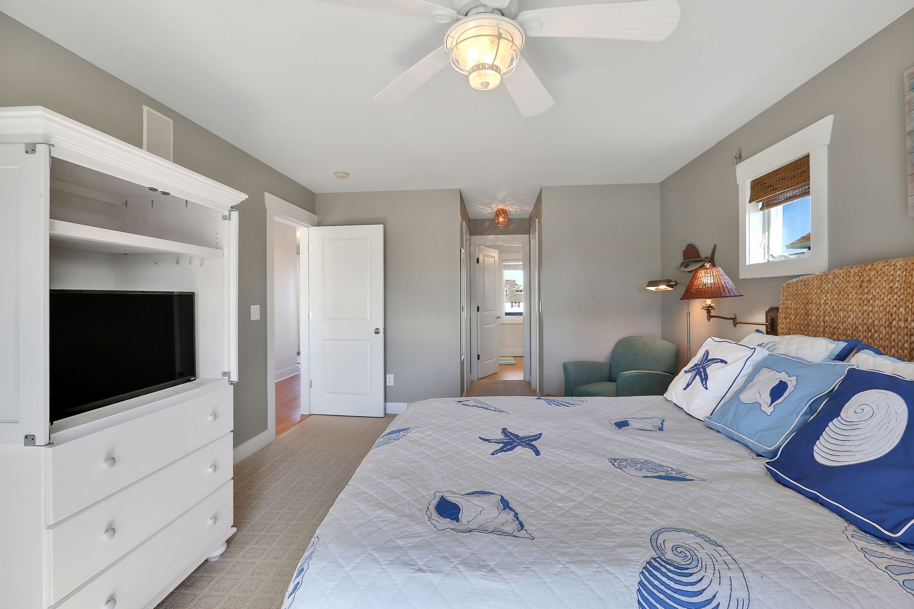 Un dormitorio con cama, televisión, ventilador de techo y ventana con persianas.