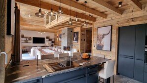 Une cuisine moderne dotée d’un grand îlot central, de poutres en bois au plafond et d’un mur d’accent en pierre.