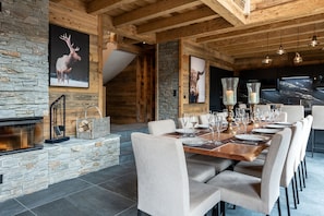 A dining area with a stone fireplace, wooden beams, and a large TV screen.