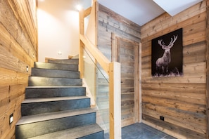 A wooden staircase with a glass railing leading to a room with a wooden wall and a deer painting.