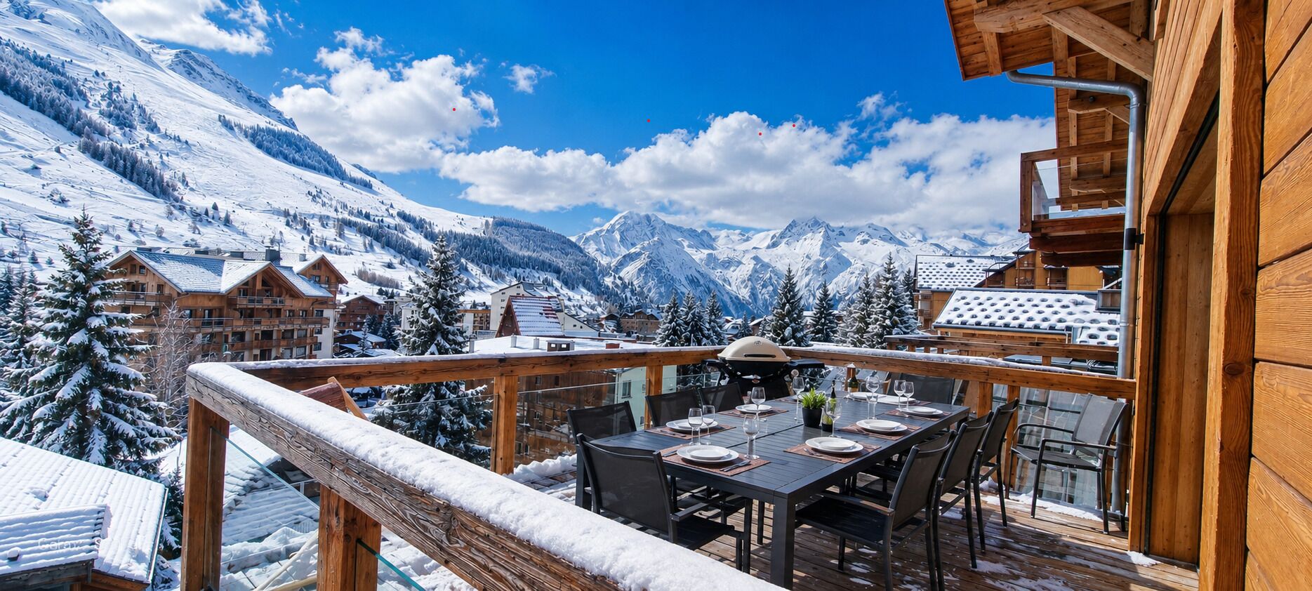 Une terrasse en bois avec une table  à manger pour quatre personnes, offrant une vue sur un paysage montagneux enneigé.