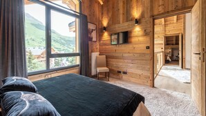 Une pièce de cabane en bois avec une grande fenêtre, un lit, une chaise et une cheminée.