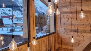 Un intérieur en bois, agrémenté de lampes suspendues et d’une grande fenêtre donnant sur un paysage enneigé.