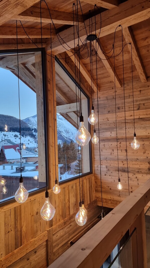 A wooden interior with hanging light bulbs and a large window overlooking a snowy landscape.