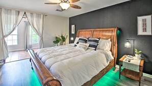A bedroom with a wooden bed, a ceiling fan, a nightstand with a lamp, and a window with curtains.