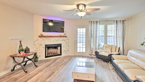 A living room with a fireplace, a ceiling fan, a sofa, and a TV mounted on the wall.