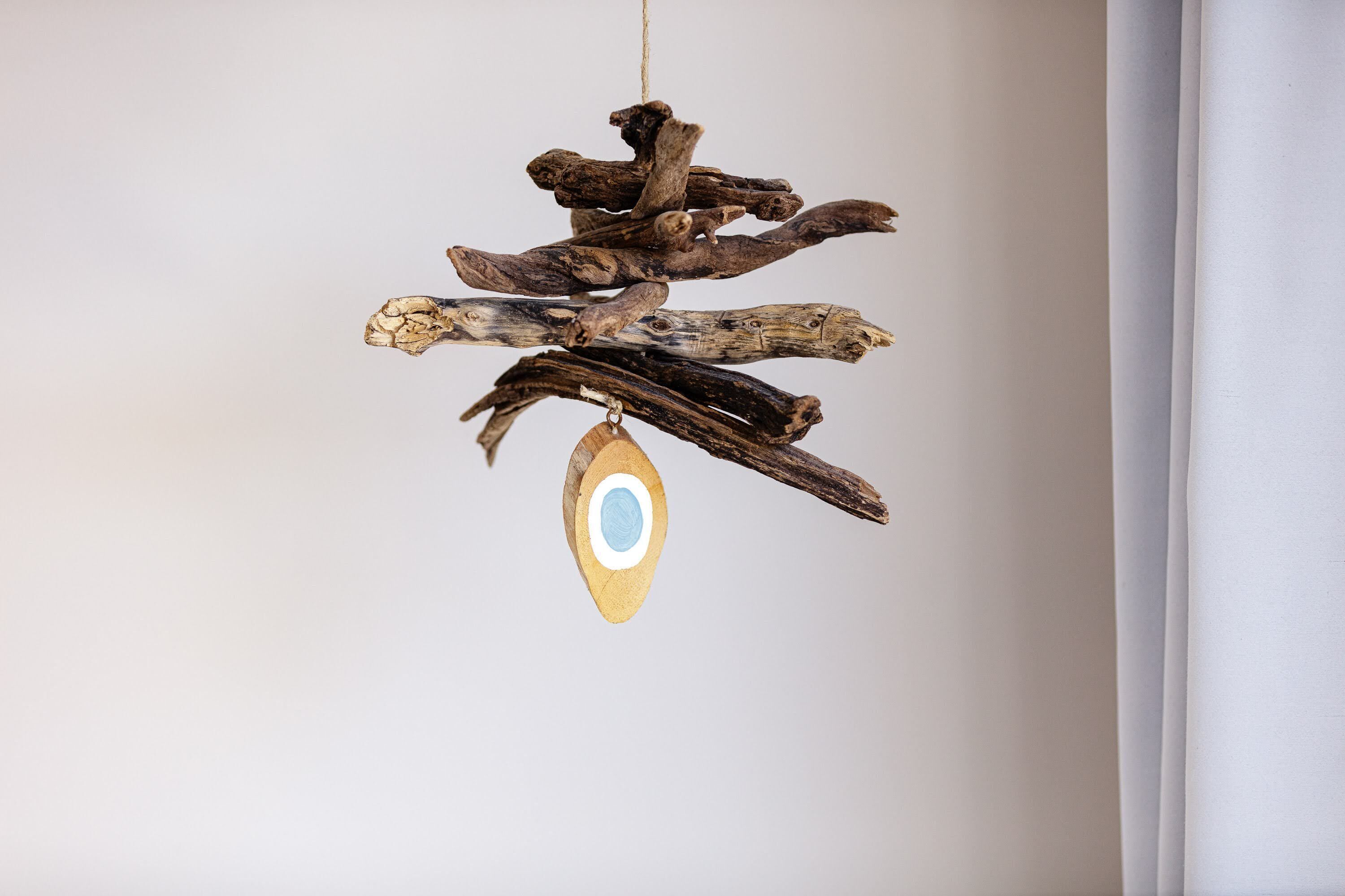 Una decoración de madera con un adorno azul y blanco en forma de ojo colgando de una rama.