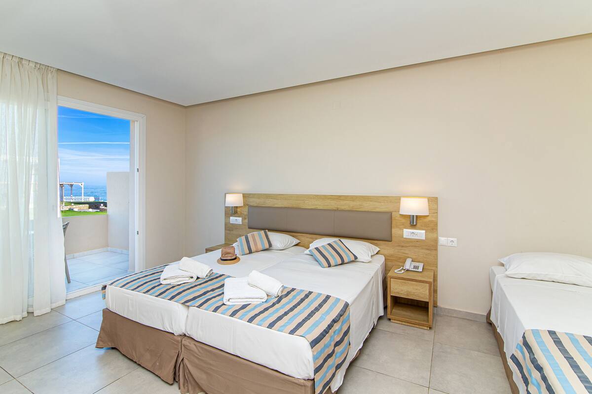 Een hotelkamer met twee bedden, een balkon en uitzicht op zee.